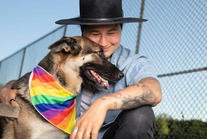 Nanook Indigenous person kneeling and smiling down at dog, who is wearing a rainbow bandana